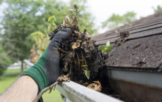 Gloved hand removing dirt from guttering