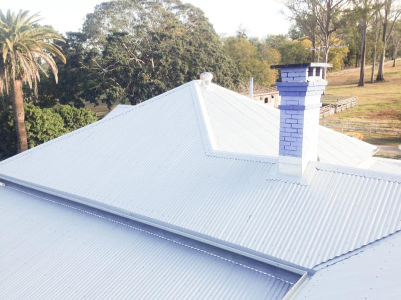 A white roof-top with a chimney and a dense forest in the background.