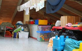 A cluttered attic with clothes, boxes, and toys scattered around.